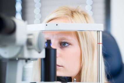 Badanie okulistyczne na lampie szczelinowej - młoda kobieta trzyma głowę na urządzeniu i patrzy się w okular. 