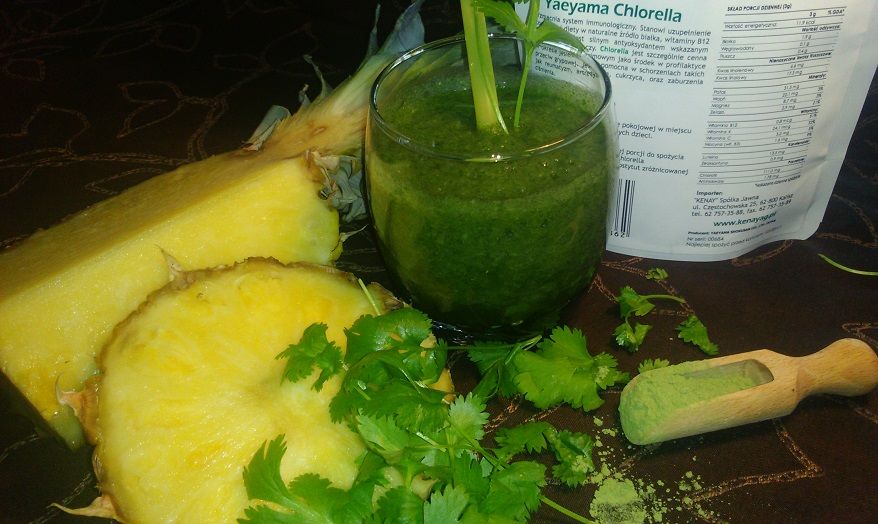 Koktajl w szklance koloru zielonego. Obok rozkrojony ananas, liście pietruszki i opakowanie chlorelli. 