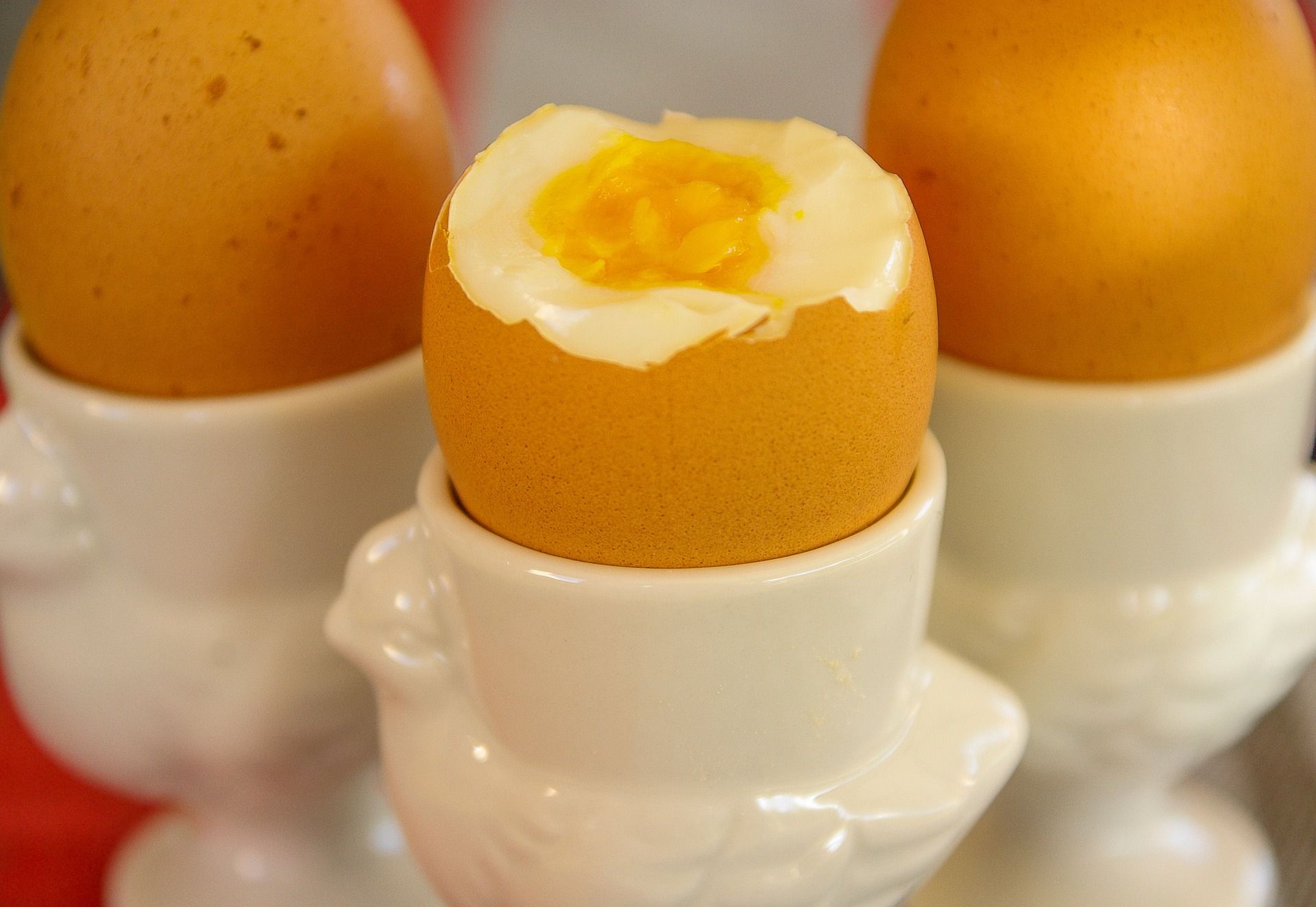 Jajka na twardo. Na zdjęciu widzimy trzy jajka w porcelanowych podstawkach. Jedno jest przekrojone. 