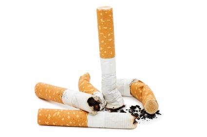 Zgaszony papieros jako symbol rzucenia palenia. Obok leżą niedopałki. Białe tło, widać tylko papierosy. 