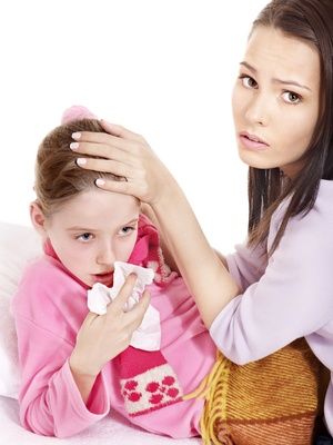 Chore dziecko z przeziębieniem, trzyma chusteczkę w ręce. Obok siedzi mama i kladzie dziecku ręke na czoło. 